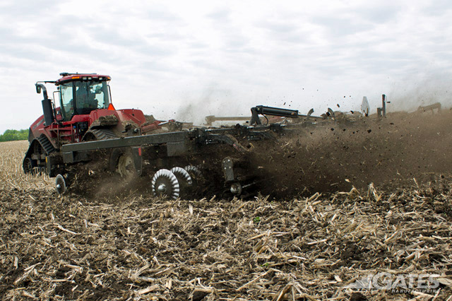 Red tractor pulling tillage equipment in a harvested field and debris in the air behind the equipment.