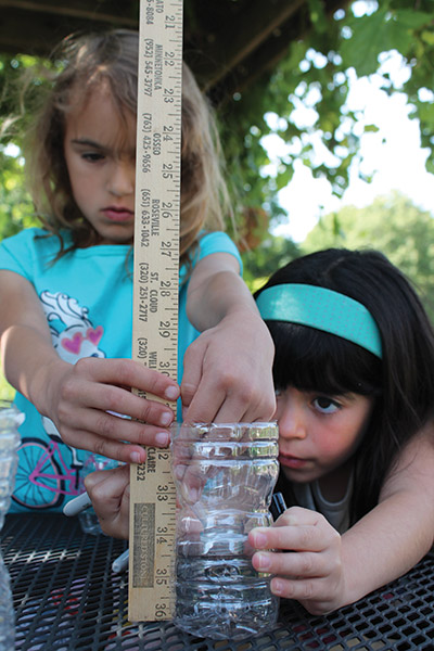 Two girls measuring a plastic bottle with a yardstick