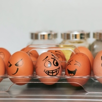 Brown eggs in clear container with faces of varying emotions drawn on them.