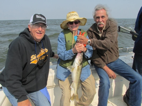 Three veterans in a boat on the water holding a fish they just caught.