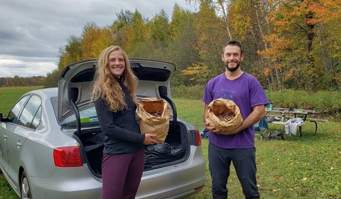 Kelly Popham and Joel Bransky holding bags of collected acorns with woods in the background.