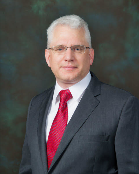 A man with glasses and gray hair wearing a suit with a red tie