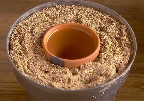 A large plastic pot filled with vermiculite with a water-filled clay pot in the center of the vermiculite.
