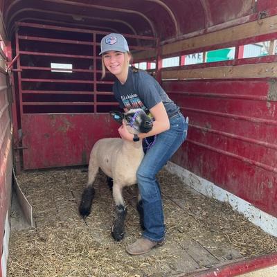 Addison Barrick and her breeding ewe wether dam in a red trailer