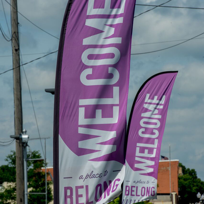 Welcome a place to belong text on two large signage flags near a Main Street road leading into a town.