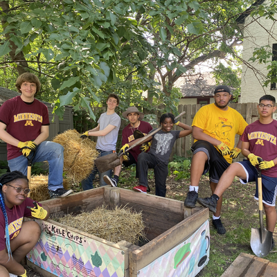 Youth posing around a raised garden bed with straw. Many are wearing University of Minnesota shirts
