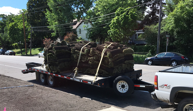 A truck and trailer with rolls of sod next to a boulevard of bare soil