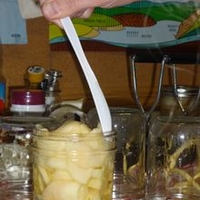 Using a plastic utensil to get air bubbles out of canning jar filled with apples.