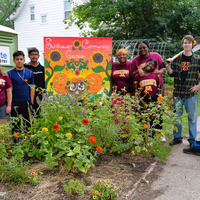 A group of UAI youth stand around a garden bed with colorful flowers