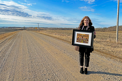 Amy Johnson stands on a gravel road holding a framed photo