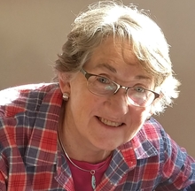 Woman in flannel shirt and glasses smiles for the camera. There is a natural light upon her hair.