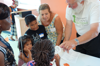 Two adults are reviewing recipes with three children in a Cooking Matters class. 